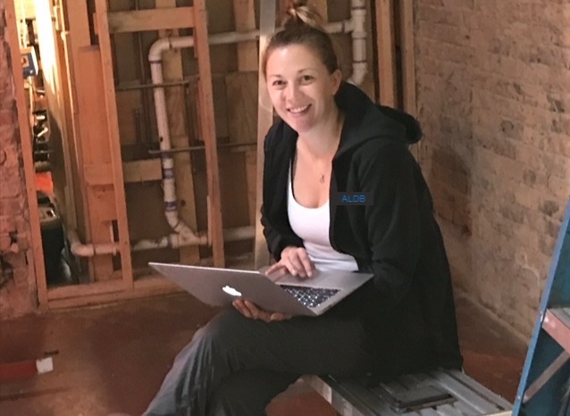 Sally Anderson Little working on a laptop at a gutted job site